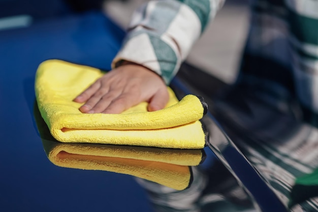 Una giovane donna che pulisce e lucida la sua auto con un panno in microfibra giallo Concetto di cura dell'auto