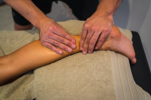 Una giovane donna che riceve un massaggio alle gambe posteriori da un fisioterapista. Physio, osteopatia
