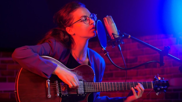 Una giovane donna che suona la chitarra e canta con luci al neon