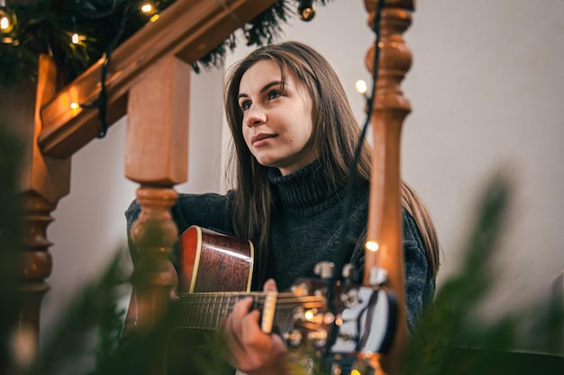 Una giovane donna che suona la chitarra seduta sui gradini di casa