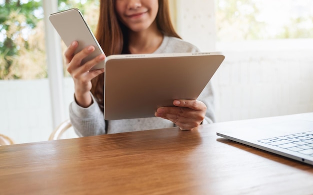 Una giovane donna che tiene e usa il telefono cellulare, il tablet pc e il computer portatile su un tavolo di legno