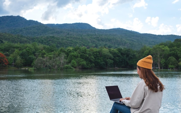 Una giovane donna che usa e lavora al computer portatile mentre viaggia sulle montagne e sul lago