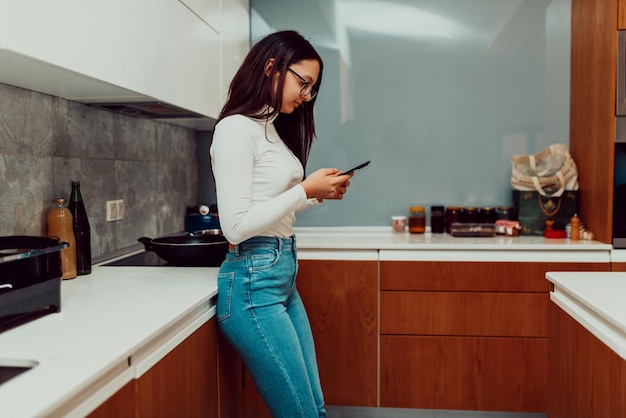 Una giovane donna che usa uno smartphone mentre cucina in cucina