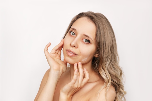 Una giovane donna con i capelli mossi che si tocca il viso con le mani applicando una crema idratante sulla pelle