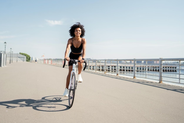 Una giovane donna con i capelli ricci in abiti sportivi in sella a una bicicletta in città Trasporto ecologico