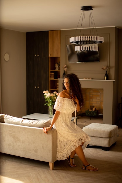 Una giovane donna con i capelli ricci si sta rilassando nel comfort della propria stanza vestita con un abito bianco fluente