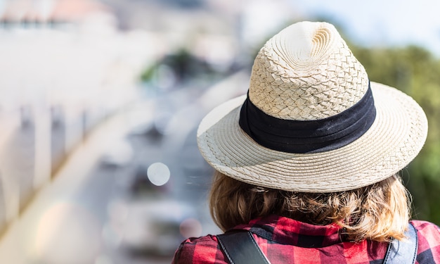 Una giovane donna con il suo cappello con uno zaino si erge su un ponte pedonale e guarda la strada