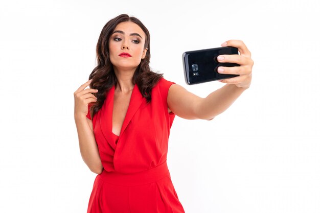 Una giovane donna con il trucco luminoso, in un abito estivo rosso sta con un telefono in mano