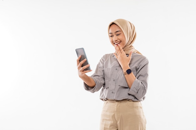 Una giovane donna con l'hijab in piedi e mette la mano davanti alla bocca mentre guarda il suo telefono