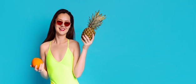 Una giovane donna con lunghi capelli scuri indossa un costume da bagno giallo e occhiali da sole rossi sta sorridendo e