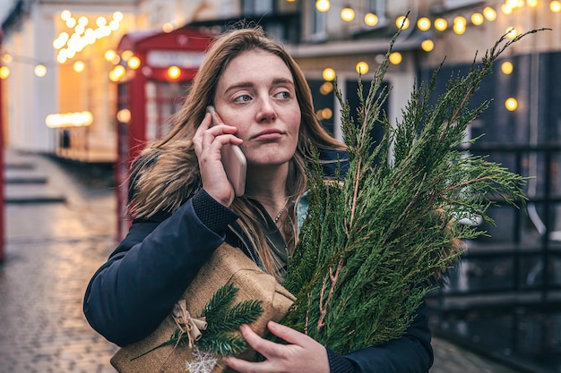 Una giovane donna con un albero di Natale e una confezione regalo che parla al telefono