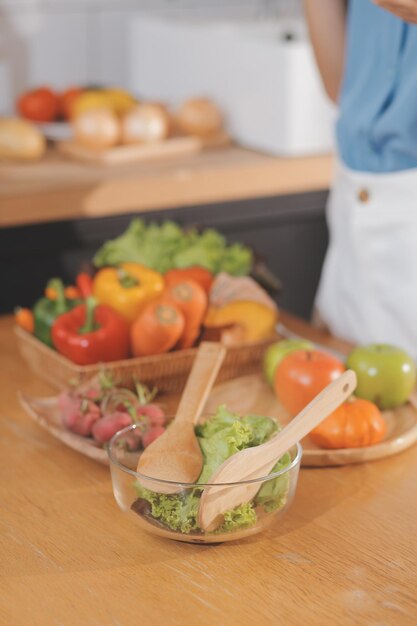 Una giovane donna con un bel viso in una camicia blu con i capelli lunghi che mangia frutta seduta in cucina a casa con un laptop e un taccuino per il relax Concept Vacation