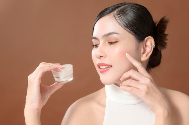 Una giovane donna con un bel viso sta tenendo la crema usando la crema del suo concetto di cura della pelle di bellezza del viso