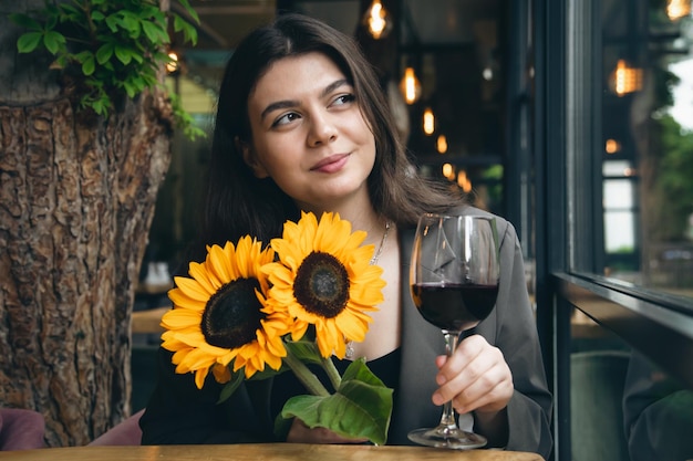 Una giovane donna con un bicchiere di vino e un bouquet di girasoli in un ristorante