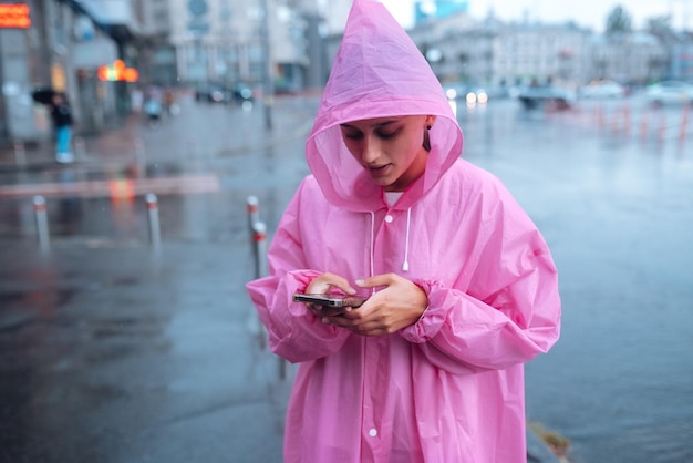 Una giovane donna con un impermeabile che guarda lo smartphone