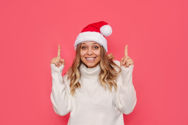 Una giovane donna con un maglione bianco e un cappello da Babbo Natale punta verso lo spazio vuoto della copia