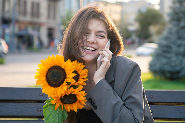 Una giovane donna con un mazzo di girasoli sta parlando al telefono al tramonto