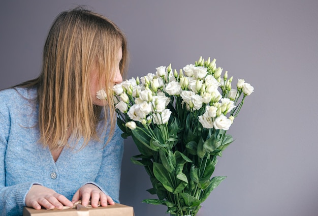 Una giovane donna con un mazzo di rose spacchetta una confezione regalo