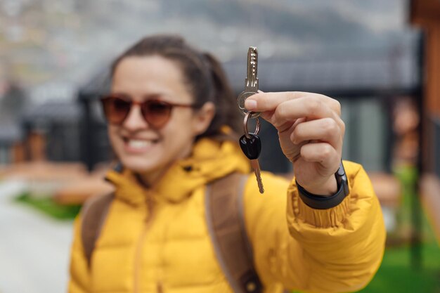 Una giovane donna con un piumino giallo tiene le chiavi di una casa per le vacanze in una zona di montagna