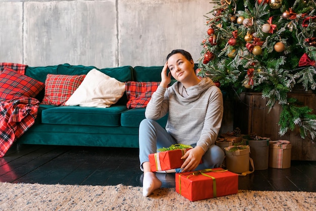 Una giovane donna con un regalo per Natale o Capodanno siede a casa sul pavimento