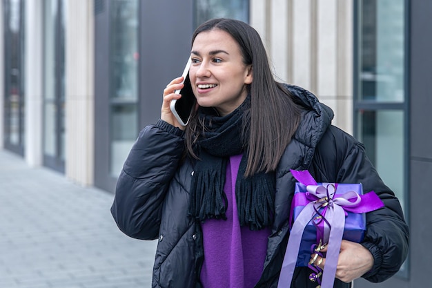 Una giovane donna con un regalo viola tra le mani parla al telefono fuori