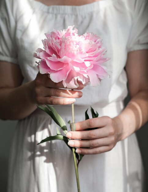 Una giovane donna con un vestito bianco tiene delicatamente in mano una peonia rosa