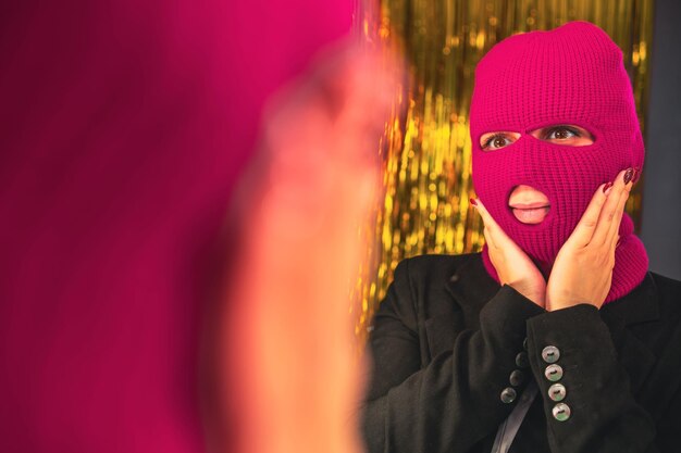 Una giovane donna con una balaclava rosa si guarda allo specchio