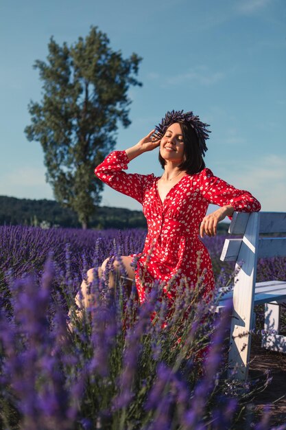 Una giovane donna con una corona in testa siede su una panchina bianca in un campo di lavanda