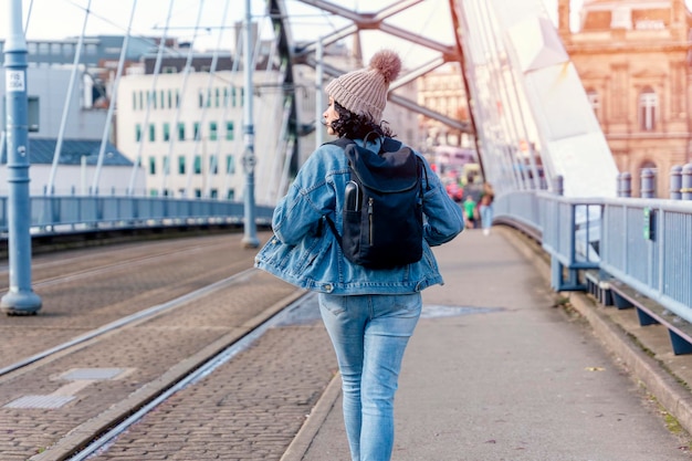 Una giovane donna con una giacca di jeans sta parlando al telefono e sta aspettando un tram alla fermata