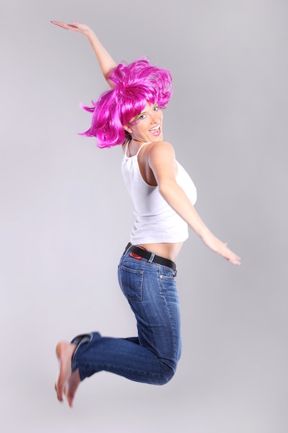una giovane donna con una parrucca viola che salta di gioia su uno sfondo chiaro