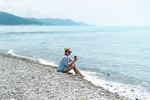 Una giovane donna con una tazza di caffè sulla spiaggia. Estate. Vacanza.