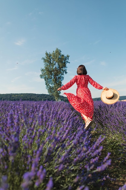 Una giovane donna corre in un campo di lavanda e tiene in mano un cappello di paglia