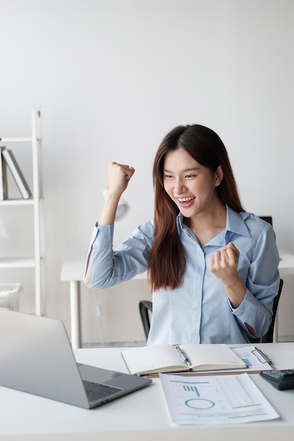 Una giovane donna d'affari asiatica di successo ed eccitata che celebra con se stessa dopo aver ricevuto la buona notizia