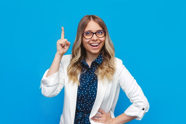 Una giovane donna d'affari bionda sorridente caucasica piuttosto intelligente con una giacca bianca e occhiali che gesticolano con il dito in su