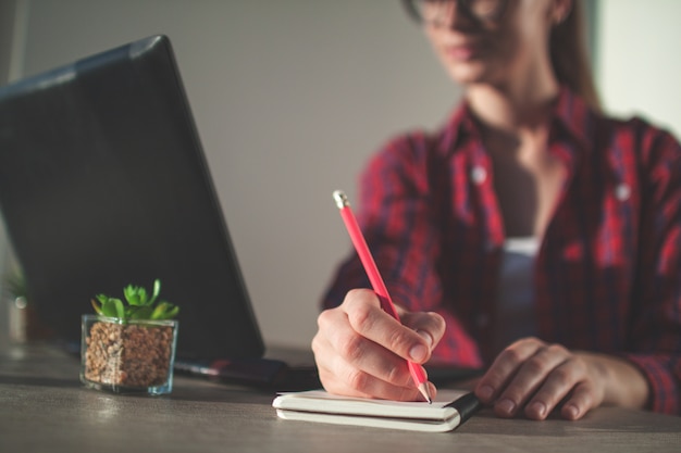 Una giovane donna d'affari che lavora online e scrive informazioni sul lavoro sul taccuino.