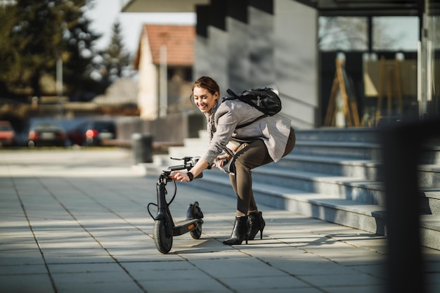 Una giovane donna d'affari che va a lavorare con uno scooter elettrico a spinta.