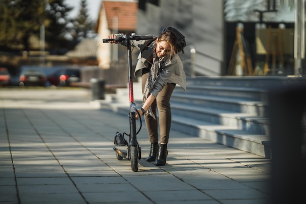 Una giovane donna d'affari che va a lavorare con uno scooter elettrico a spinta.