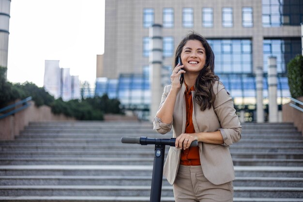 Una giovane donna d'affari con uno scooter elettrico che va al lavoro e utilizza uno smartphone