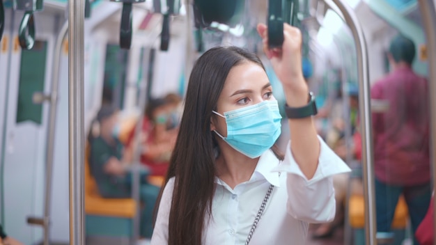 Una giovane donna d'affari indossa la maschera per il viso nei trasporti pubblici, viaggi sicuri, concetto di protezione covid-19.