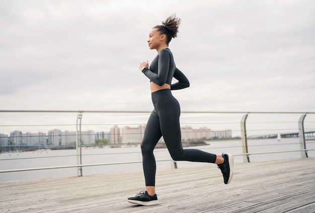 Una giovane donna dai capelli ricci in un abito nero sportivo e scarpe da corsa che fanno jogging sul fitness di strada