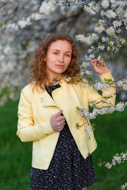 Una giovane donna dai capelli rossi sta annusando i fiori primaverili nel parco