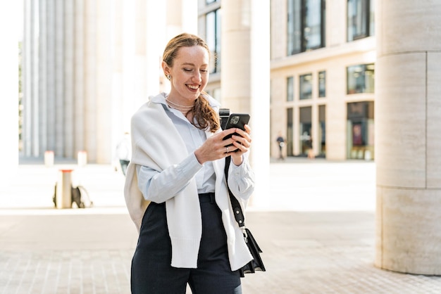 Una giovane donna di successo in abiti formali che va in ufficio Usa il telefono per scrivere un messaggio