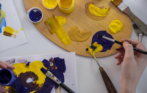 Una giovane donna dipinge con la tempera a casa Hobby di disegnare con la tempera Un angolo ravvicinato Pittura brillante e il processo di disegno con la tempera