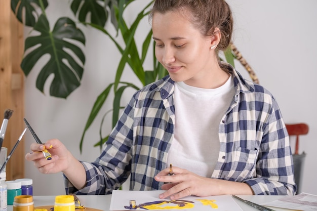 Una giovane donna disegna con guazzo su un foglio bianco Disegno di meditazione Una donna sceglie un pennello adatto per il disegno