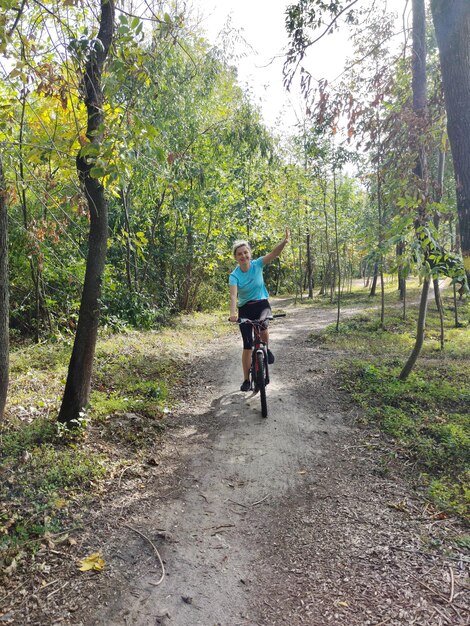 Una giovane donna è in bicicletta nel parco e agita la mano ricreazione attiva in natura