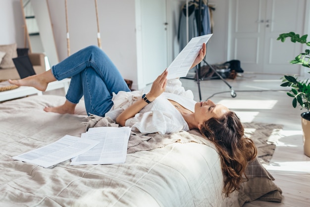 Una giovane donna è sdraiata su un letto in camera da letto a leggere.