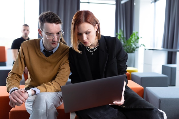 Una giovane donna e un uomo sono seduti con i laptop e discutono di progetti aziendali in ufficio