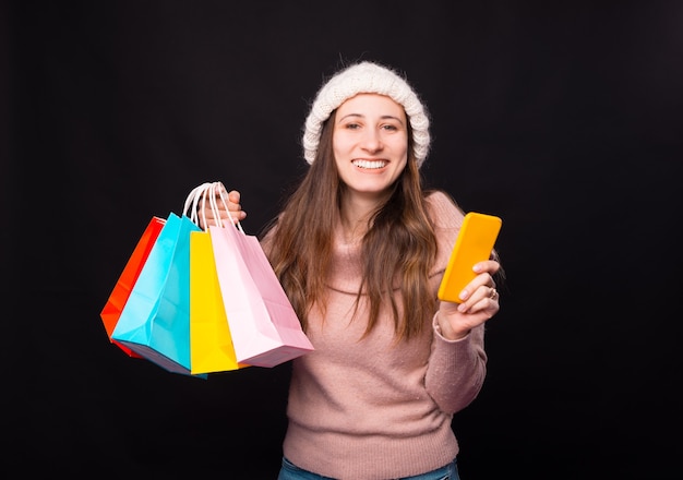 Una giovane donna eccitata per il suo acquisto online. Ha in mano alcune borse colorate e il suo telefono.