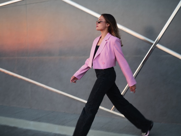 Una giovane donna elegante con una giacca rosa alla moda e occhiali da sole