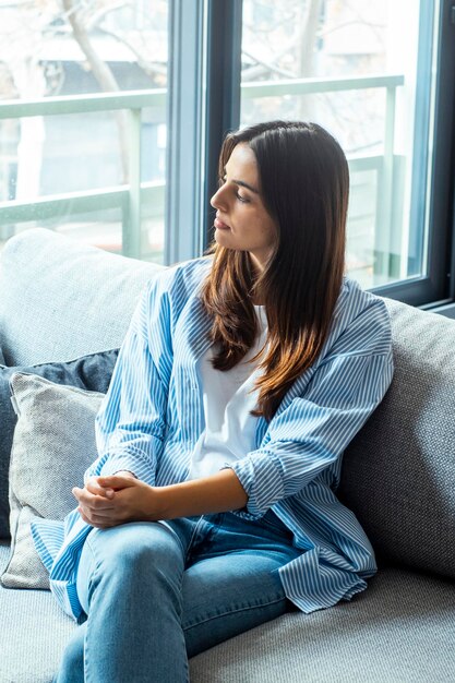 Una giovane donna esausta, frustrata, che tocca la fronte, seduta sul divano, sola, che soffre di forti mal di testa o emicrania, una ragazza preoccupata, che pensa a problemi, al divorzio o alla rottura, perduta nei suoi pensieri.